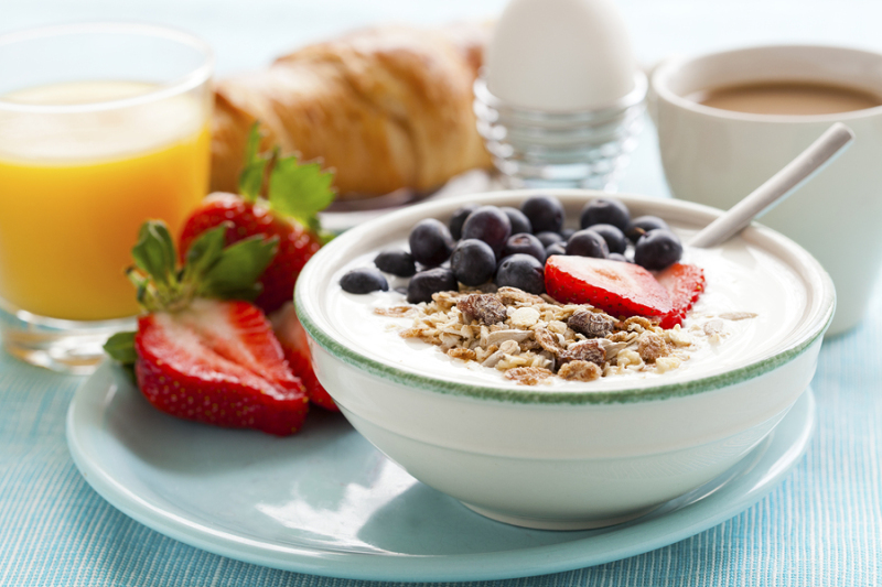 Bowl of muesli with yoghurt, strawberries and blueberries, boiled egg, orange juice, croissant and coffee for healthy breakfast